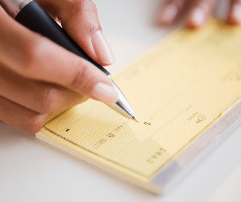 Mano escribiendo cheque nacional para cambio por efectivo